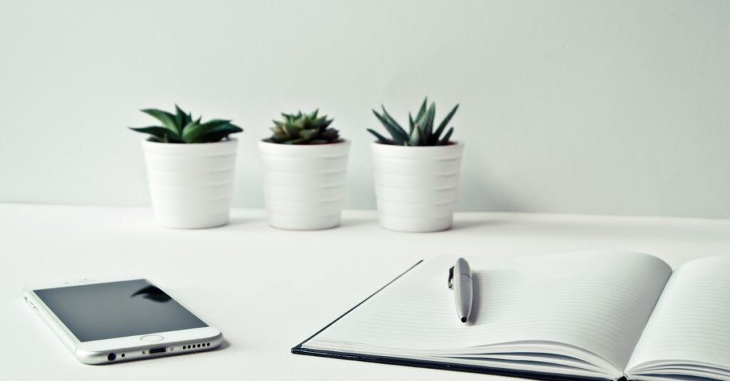 pexels-photo-796602-796602-1 A clean, minimalist workspace featuring a smartphone, open notepad, pen, and potted succulents.